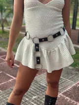 Cinturón negro de cuero sintético con múltiples aros metálicos plateados unidos por tiras de cuero. Incluye un gancho para ajuste regulable.