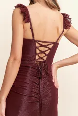 Vestido largo de corte sirena confeccionado en tejido brillante y elástico. Presenta un diseño ajustado con frunces en el torso, escote cuadrado y breteles con detalle de encaje tipo eyelash.