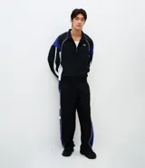 Campera deportiva de poliamida con diseño de bloques de color en negro, blanco y violeta. Presenta cuello alto, cierre frontal con cremallera, puños y ruedo elásticos, y forro interior de poliéster.