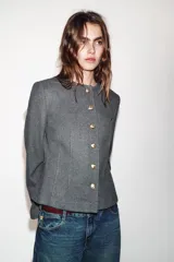 Blazer de corte entallado con cuello redondo, manga larga y hombreras. Presenta cierre frontal con botones dorados y una textura sutil en la tela.