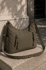 Cartera hobo gris de tela suave y liviana, con bolsillos frontales con cierre y tiradores trenzados, correa ajustable y compartimento principal con cierre.