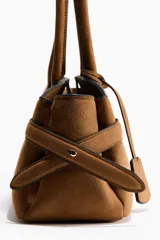 Cartera de hombro color tostado, con doble asa superior y detalle de tiras laterales ajustables. Cuenta con cierre magnético y etiqueta colgante.