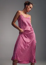 Vestido midi de tejido satinado en color rosado con estampado de lunares marrones. Presenta un diseño recto, cuello escotado y tirantes finos dobles que se cruzan en la espalda abierta.