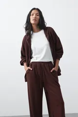 Pantalón de corte holgado y pierna ancha, con cintura elástica ajustable mediante cordón. Presenta bolsillos laterales y costuras verticales decorativas que recorren el frente de las piernas.