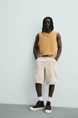 Bermuda de algodón color beige claro con efecto lavado y estampado abstracto en tonos grises. Diseño de corte relajado con cierre frontal de botón y cremallera, bolsillos delanteros y bolsillos traseros de plastrón.