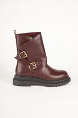 Bota corta de símil cuero color bordó, estilo biker, con caña media y recortes asimétricos decorados con dos hebillas metálicas doradas. Posee suela track gruesa y cierre lateral.
