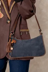 Cartera tipo baguette de gamuza azul marino con bordes y correa de cuero color chocolate. Incluye un colgante decorativo con borla de cuero y cuentas de madera.
