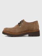 Zapato bajo de mujer color camel, estilo mocasín o derby, confeccionado en gamuza. Presenta suela gruesa de plataforma color marrón oscuro con costura visible en color claro. El sistema de ajuste es mediante cordones marrones que pasan por ojales metálicos tipo gancho.