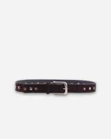 Cinto de gamuza color marrón oscuro, decorado con tachas metálicas plateadas y doradas a lo largo de toda la pieza. Cuenta con una hebilla metálica clásica de diseño rectangular.