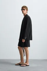 Blazer negra de corte relaxed fit, confeccionada en tejido con mezcla de viscosa. Tiene cuello con solapas de pico, manga larga con puños abotonados, bolsillos de vivo en pecho y cadera, abertura en el centro de la espalda y cierre frontal cruzado con botones.