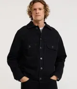 Campera de hombre de jean negro, modelo regular, con cuello inglés, abotonado frontal, dos bolsillos con solapa en el pecho y manga larga ajustada.