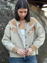 Campera color beige con apliques de cuero marrón en hombros y frente, corte recto y cierre con botones.