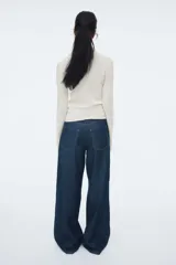 Top ajustado de punto acanalado suave, color beige, con cuello alto y mangas largas acampanadas.