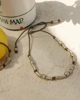 Collar artesanal compuesto por piezas metálicas irregulares con acabado dorado, ensartadas en un cordón de hilo de algodón natural. Presenta un sistema de nudo corredizo para ajustar el largo.