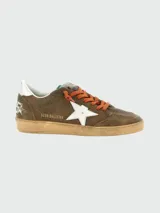 Zapatillas deportivas Golden Goose modelo Ball Star, estilo retro de baloncesto. Cuerpo de gamuza marrón, con estrella lateral blanca y talón plateado. Cordones naranjas y suela de goma desgastada.