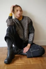 Chaqueta corta con cuello alto, mangas largas de cuero sintético negro y cuerpo de tweed en tonos blanco y negro. Cierre frontal con botones a presión.