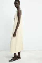 Vestido midi de color beige con diseño jacquard sutil. Presenta un escote en pico pronunciado, tirantes anchos y un bajo con acabado asimétrico.