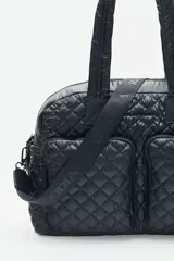 Bolso tipo shopper color marrón con diseño matelassé. Tiene doble asa corta y correa larga desmontable. Incluye llavero de corazón y dijes desmontables, y compartimento interior para notebook.