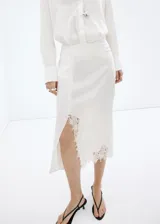 Falda midi de tiro medio color blanco, de corte recto con abertura lateral pronunciada y detalles de encaje en el borde y la abertura.
