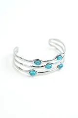 Brazalete rígido de metal plateado con diseño de tres tiras onduladas adornadas con piedras turquesas ovaladas.