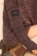 Polerón tejido de punto con efecto jaspeado en tonos oscuros, de corte oversize y manga larga. Presenta un parche rectangular con el logo de la marca en la manga.