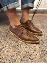 Zapato acordonado color marrón, con suela plana y cordones finos.