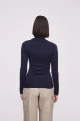 Polera de tejido de punto fino en color azul marino, con cuello alto y mangas largas. Presenta un ajuste al cuerpo y terminaciones acanaladas en cuello, puños y ruedo.