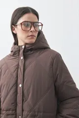 Campera puffer negra con diseño acolchado, capucha integrada y cierre frontal con botones a presión. Presenta puños elásticos y costuras decorativas en el frente.