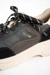 Zapatilla urbana de cuero con diseño de paneles en tonos negro, marrón oscuro y beige. Presenta una suela de plataforma robusta en color beige y cordones jaspeados.