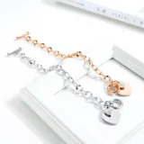 Pulsera de eslabones gruesos en acero quirúrgico color plata, con dijes colgantes en forma de corazón, uno liso y otro con incrustaciones.