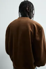 Cazadora bomber negra de corte regular fit, confeccionada en tejido efecto ante. Cuenta con cuello, puños y bajo en rib elástico, manga larga, bolsillos de vivo en la cadera y un bolsillo interior. Cierre frontal con cremallera.