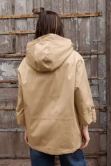 Parka liviana color beige con capucha, cierre frontal con botones, bolsillos delanteros con tapa y ajuste en la cintura. Presenta mangas con puños vueltos y detalle de botones.