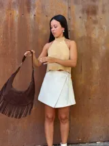 Cartera de hombro tipo hobo confeccionada en cuero gamuzado color chocolate, con detalle de flecos largos en la parte inferior y correa ajustable con hebilla metálica.