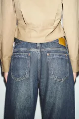Jeans de tiro medio con corte relax fit y pernera holgada. Presenta diseño de cinco bolsillos, cierre frontal con cremallera y botón, y bajo con vuelta marcada.