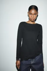 Top de manga larga en tejido suave color gris, con cuello redondo y bajo asimétrico decorado con encaje negro a tono. Presenta detalles de encaje negro en los puños.