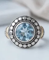 Anillo de plata y oro con circonia central redonda en tono aguamarina, rodeada de detalles texturizados.