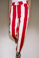 Jeans de tiro medio y corte tapered, con diseño de rayas verticales a contraste en color rojo y blanco. Cuenta con trabillas en la cintura, cinco bolsillos y cierre frontal con cremallera y botón metálico.