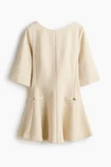 Vestido corto de tejido bouclé color beige, con escote redondo, espalda en V y mangas francesas. Cuenta con bolsillos decorativos con botones dorados en la cintura y falda con vuelo.