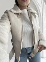 Chaqueta color crema con cuello y puños de piel sintética, cierre frontal con cremallera y cinturón ajustable en la cintura.