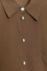 Camisa oversize de algodón con cuello solapa, manga larga y cierre frontal con botones. Presenta un bolsillo de plastrón en el frente y un diseño de corte amplio con ruedo redondeado.