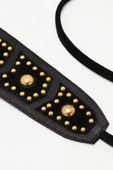 Cinturón tipo faja de cuero vacuno negro, con diseño ancho y decorado con tachas metálicas doradas. Incluye tiras largas con borlas en los extremos para anudar en la cintura.