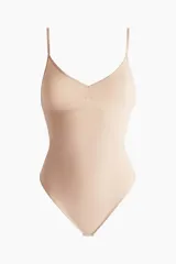 Body modelador tipo tanga color beige, con efecto vientre plano. Presenta copas forradas con sección en punto menguado para realce y sujeción suave, sin aros. Cuenta con breteles ajustables y cierre inferior con botones a presión ocultos. Diseño sin costuras para mayor comodidad.
