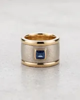 Anillo ancho confeccionado en plata 925 con lámina de oro 18k en los bordes y acabado texturizado, decorado con una circonia cuadrada central de color azul.