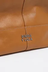 Bolso de mano Bimba y Lola modelo Paper mediano, confeccionado en cuero color tostado con estructura blanda, asas superiores y correa de hombro ajustable en color beige. Presenta costuras visibles, logo metálico de la marca en la parte inferior y cierre principal.