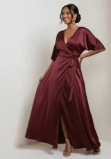 Vestido largo tipo kimono confeccionado en satén color bordó, con escote en V cruzado, mangas amplias y lazo ajustable en la cintura. Presenta una falda fluida con abertura lateral.