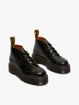 Botas Dr. Martens modelo Church Quad de cuero negro, con plataforma gruesa acanalada, costuras amarillas contrastantes y cordones negros.