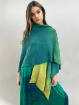 Ruana de lana merino con diseño en degradé de tonos verdes. Presenta un cuello plisado artesanalmente en fieltro de lana merino, ofreciendo una textura suave y un acabado elegante.