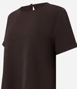 Blusa blanca de poliéster con cuello redondo, mangas cortas, cierre trasero en forma de gota, pequeñas aberturas laterales y acabados en pespuntes en las mangas y el cuello.