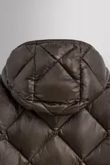 Campera puffer verde oliva acolchada con diseño de rombos, capucha y cierre frontal con cremallera. Incluye bolsillos laterales con cierre. Relleno de plumón y plumas.