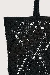 Bolsa tipo tote tejida en crochet con diseño de diamantes en color negro. Cuenta con doble asa superior trenzada y un detalle de etiqueta de cuero sintético color suela colgando de una de las asas.